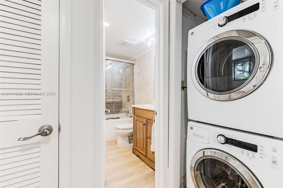 Laundry area featuring a stacked washer and dryer unit, louvered closet door, and wood-finish flooring