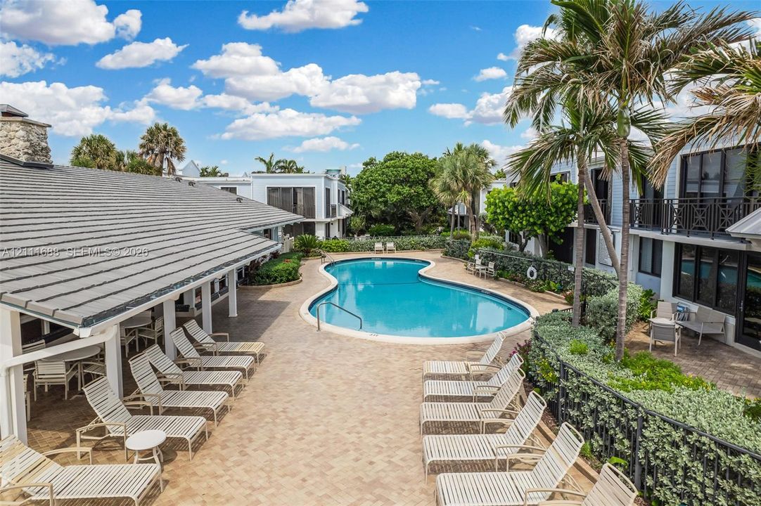 Curved swimming pool featuring a concrete paver pool deck and a covered patio area with support columns