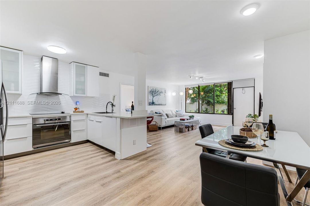 Kitchen featuring flat-panel cabinetry, stainless steel range hood, stone-finish countertops, textured backsplash, and wood-finish flooring
