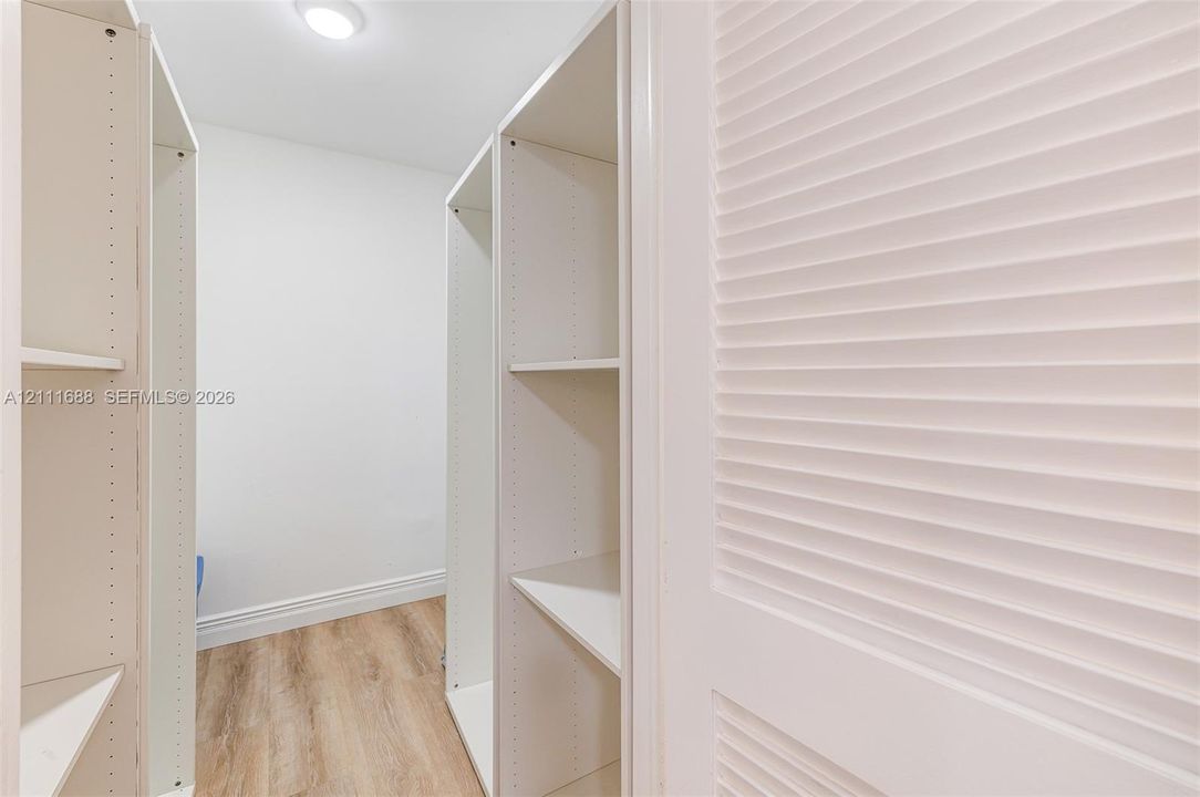 Walk-in closet featuring white built-in shelving, wood-finish flooring, and white louvered doors