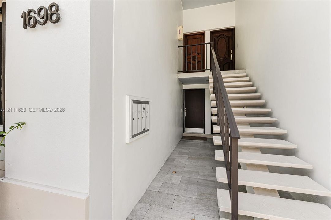 Exterior entryway featuring stone-finish flooring, a metal staircase with a matching handrail, and multiple wood-panel entry doors