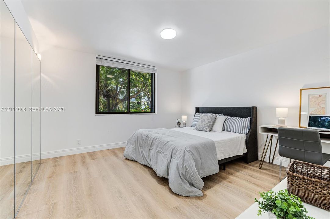 Wood-finish flooring, full-wall mirrored closet doors, and a large window with greenery exterior