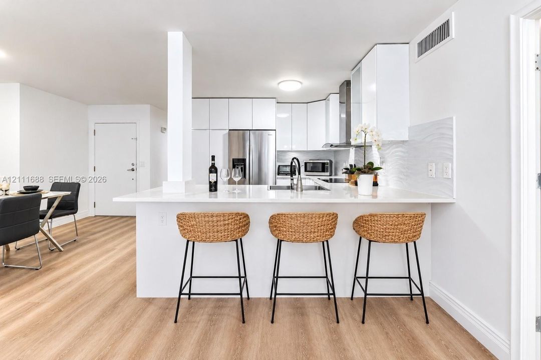 Kitchen featuring flat-panel white cabinetry, white stone-finish countertops, stainless steel appliances, textured tile backsplash, and light wood-finish flooring