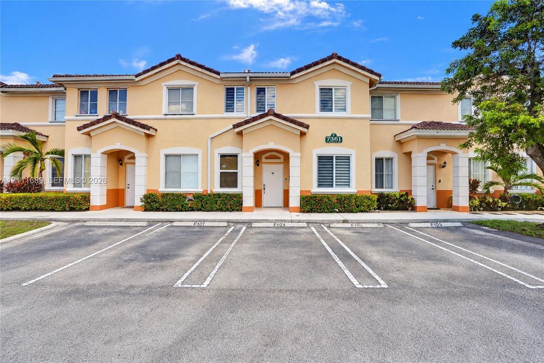 Two-story exterior featuring a stucco façade, gabled rooflines, covered entryways with columns, and dedicated asphalt parking spaces