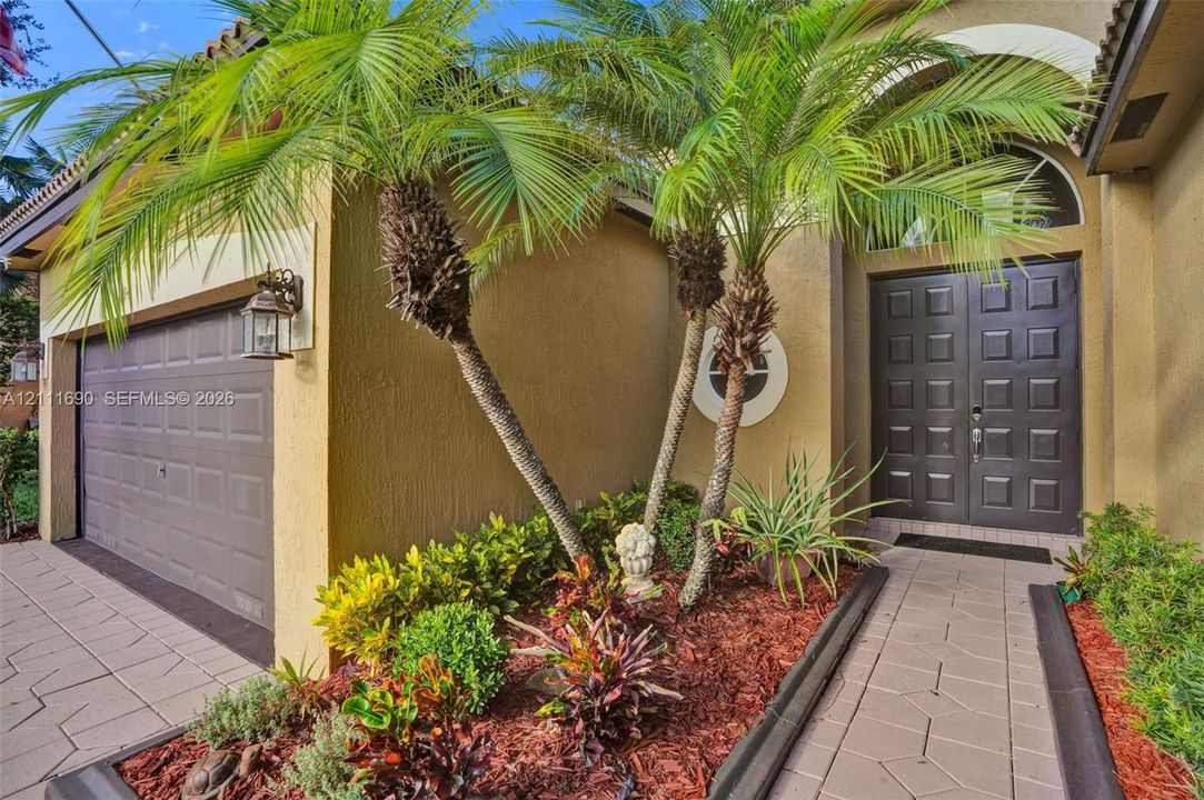 Stucco exterior featuring dual palm trees, a paver walkway, a raised-panel double front entry door, and a multi-section garage door