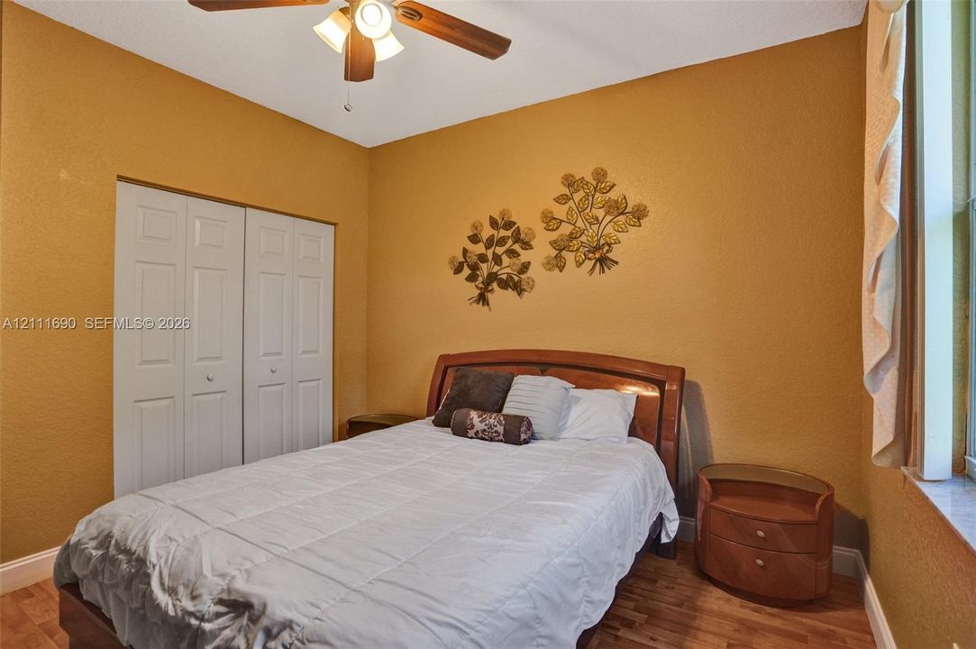 Room featuring wood-finish flooring, dual-panel closet doors, and a ceiling fan with integrated lighting
