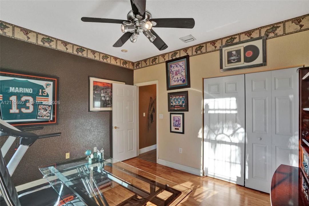 Room featuring wood-finish flooring, a multi-blade ceiling fan with integrated lighting, and dual bi-fold closet doors