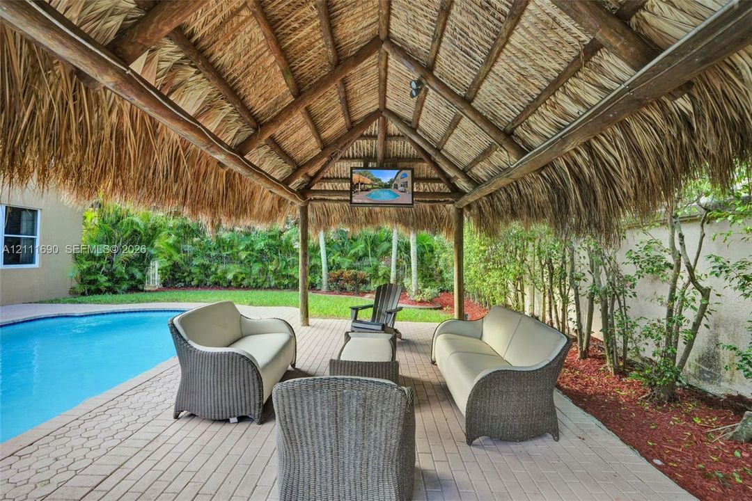 Outdoor covered pavilion featuring a thatched roof, timber framing, paved patio flooring, and a built-in television