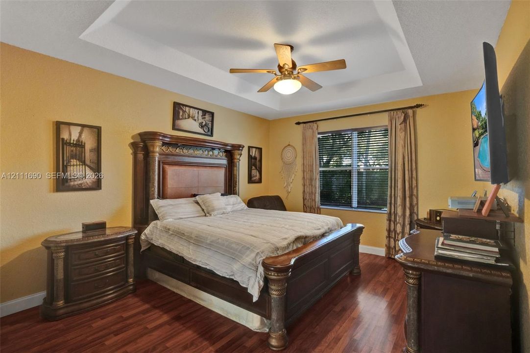 Tray ceiling with a central ceiling fan and wood-finish flooring