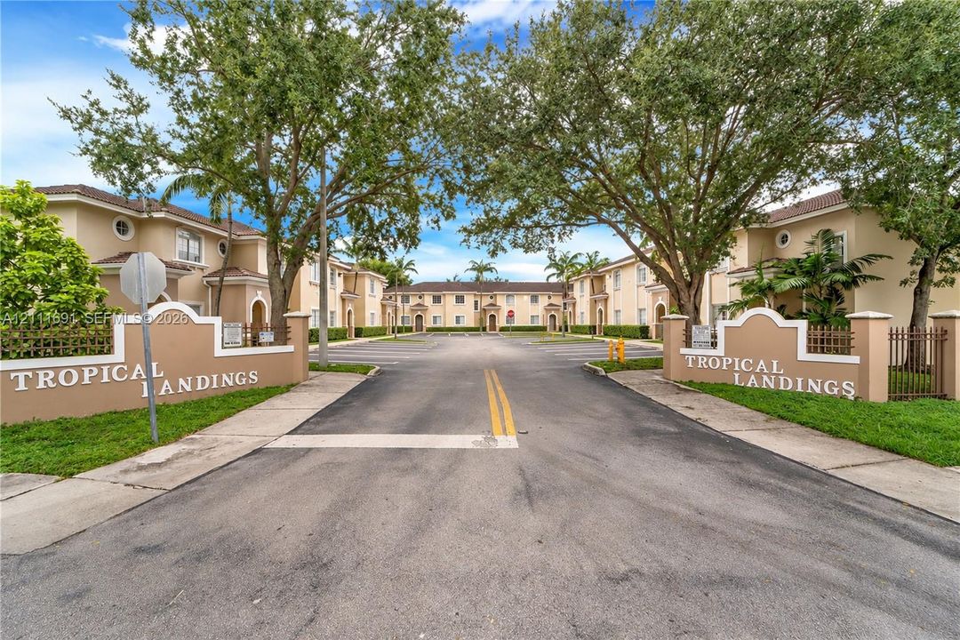 Stucco exterior multi-unit complex featuring dual monument signage, paved entry drive, and mature tree canopy