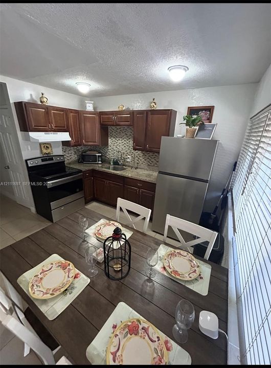 Kitchen featuring dark wood cabinetry, stone-finish countertops, decorative mosaic tile backsplash, and stainless steel appliances