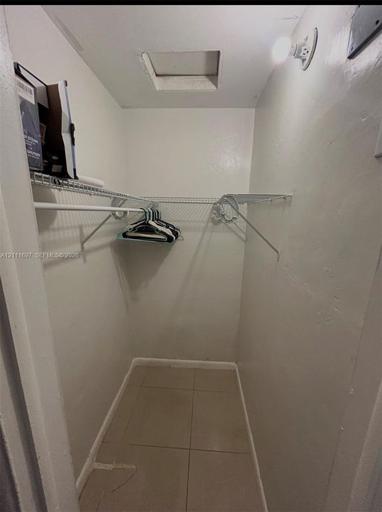 Storage area featuring large-format ceramic floor tiles, wall-mounted wire shelving, and an attic access panel