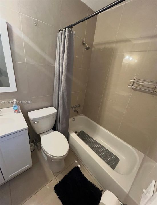 Full-height neutral wall tiling, integrated white vanity with storage, soaking tub with shower head, and wall-mounted metal shelving