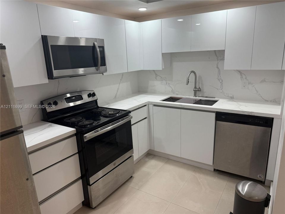 Kitchen featuring high-gloss white cabinetry, stone-surface countertops with backsplash, stainless steel appliances, and a pull-down kitchen faucet