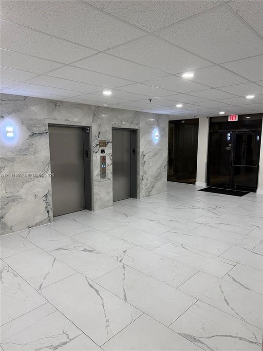 Elevator lobby featuring stone-paneled walls, large-format tiled flooring, recessed ceiling lighting, and dual metallic elevator doors