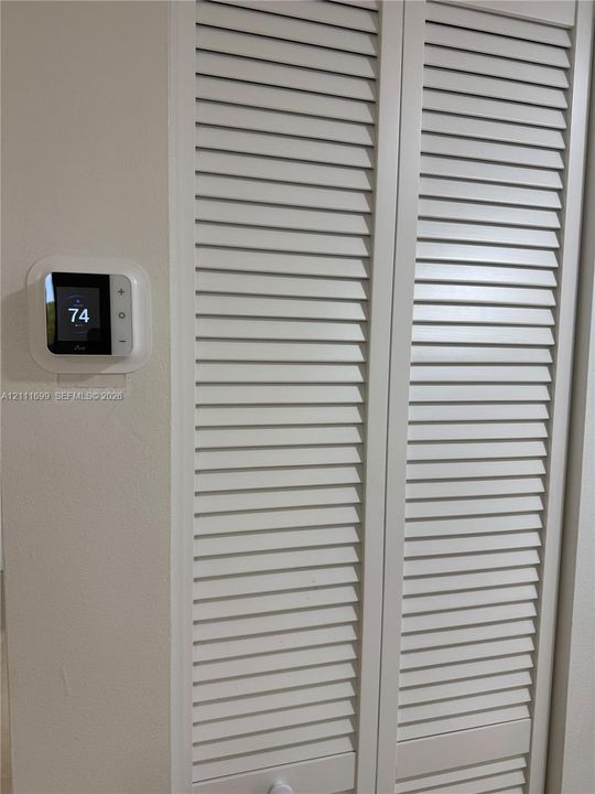 Digital smart thermostat and white bi-fold louvered closet doors
