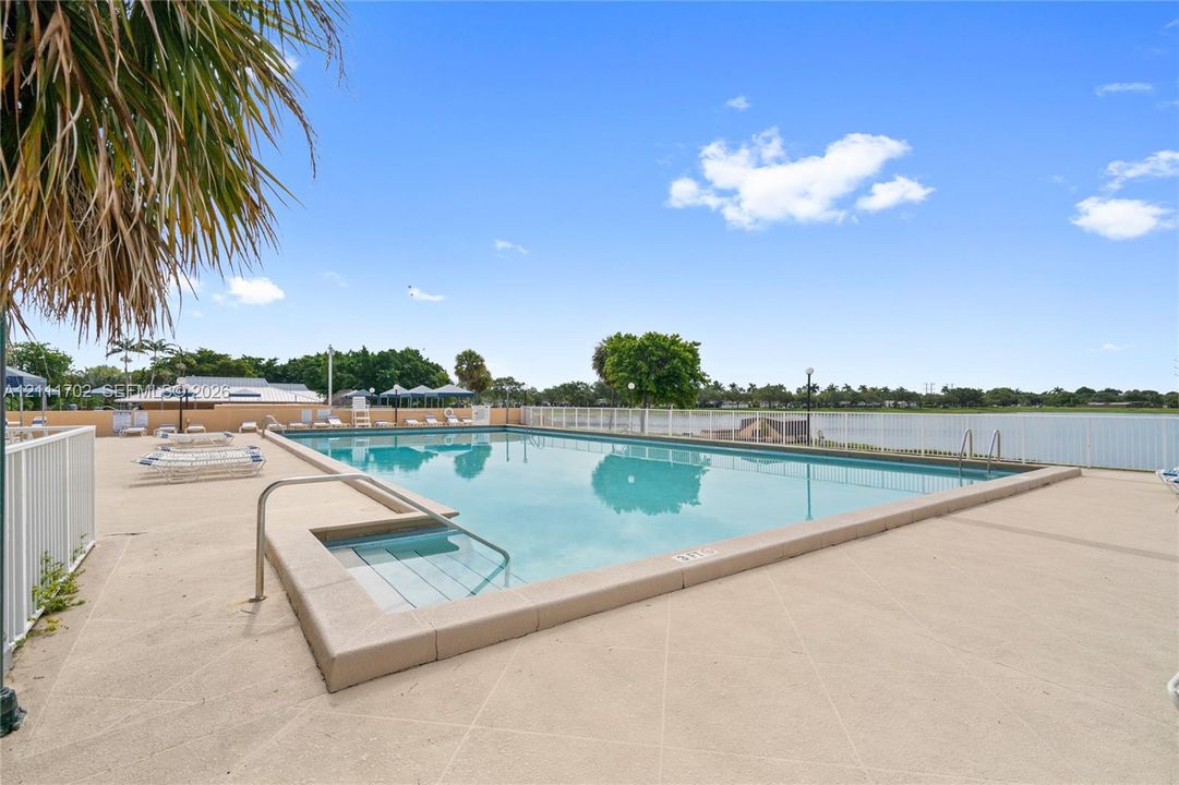 Outdoor swimming pool featuring a concrete deck, built-in entry steps, metal safety railing, and perimeter fencing
