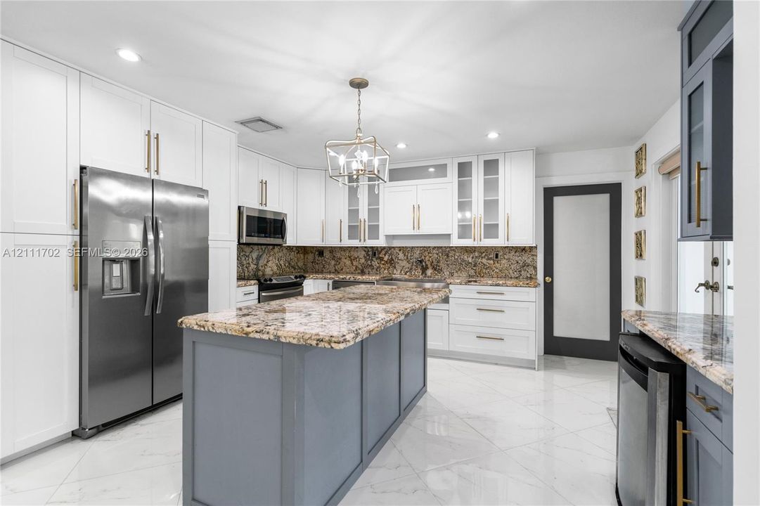 Kitchen featuring white shaker-style cabinetry, a contrasting gray center island, stone-surfaced countertops, stainless steel appliances, and tile flooring