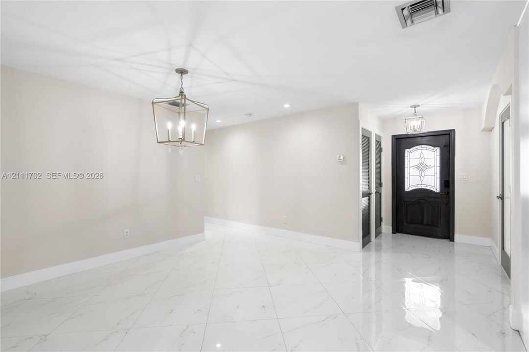 Large-format polished tile flooring, lantern-style chandelier, recessed lighting, and a solid wood entry door with decorative glass inlay
