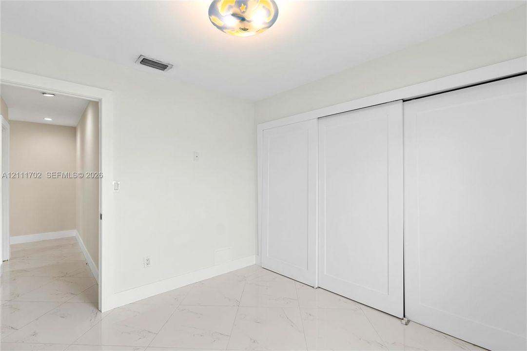 Neutral tile flooring with a veined pattern, large sliding panel closet doors, and a central ceiling-mounted light fixture