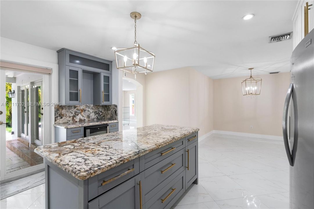Kitchen island with stone countertop, gray shaker-style cabinetry, metallic pendant lighting, and polished flooring