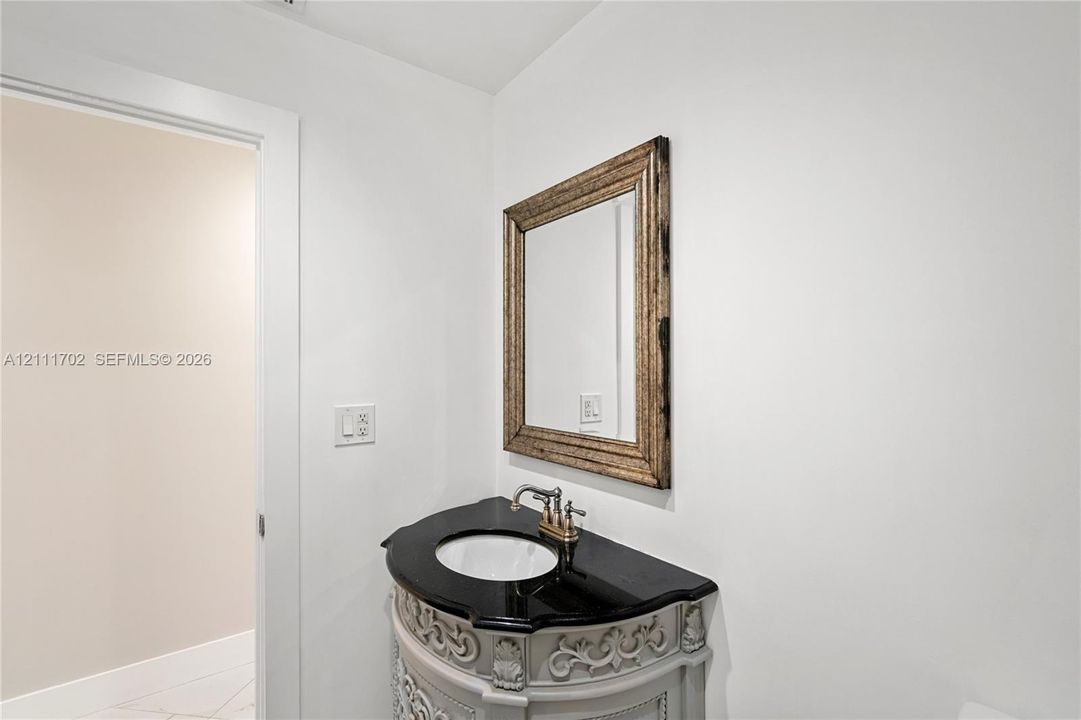 Ornate light-grey vanity with decorative carved detailing, black stone countertop, integrated undermount sink, brushed-metal faucet, and wall-mounted framed mirror