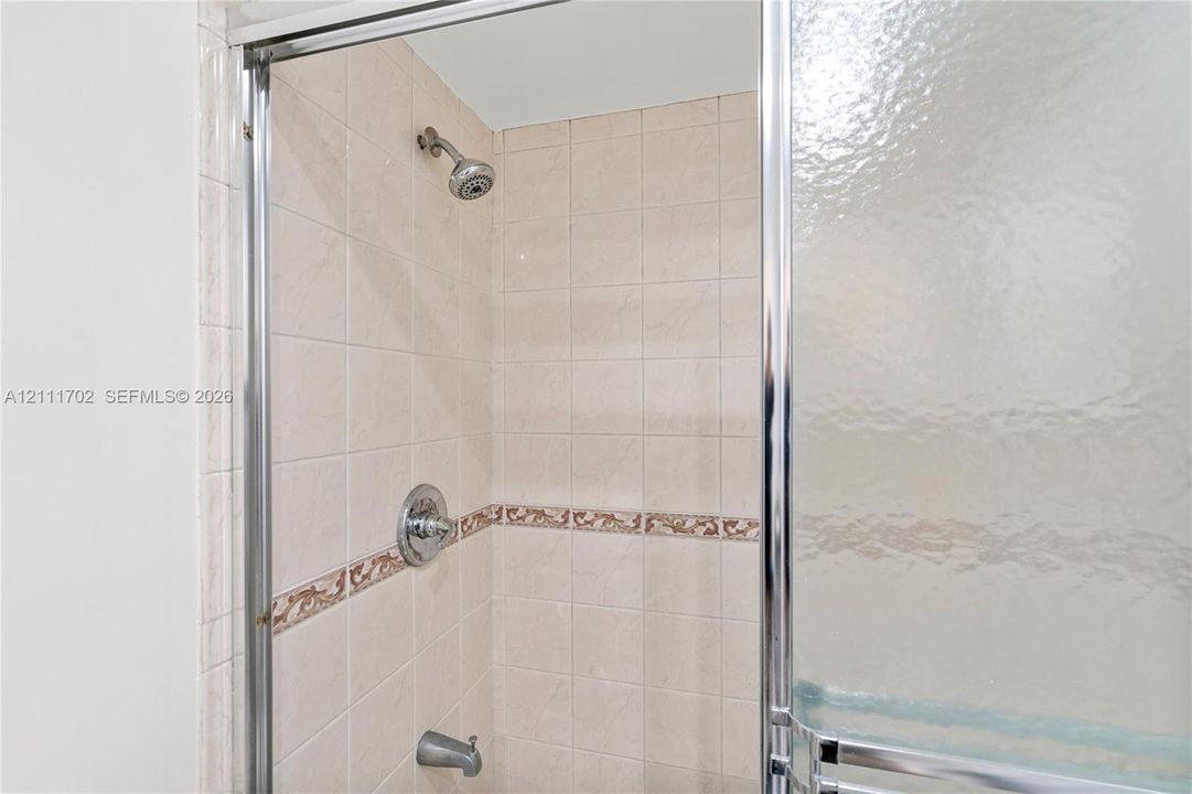 Shower stall featuring square wall tile, decorative inset tile trim, chrome shower head, chrome single-handle mixing valve, and a metal-framed glass sliding door