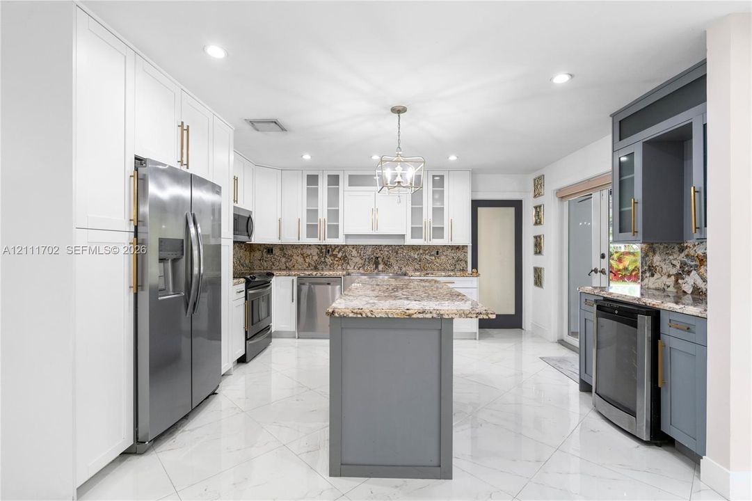 Kitchen featuring white and gray shaker-style cabinetry, stone countertops, central island, stainless steel appliances, and large-format tile flooring