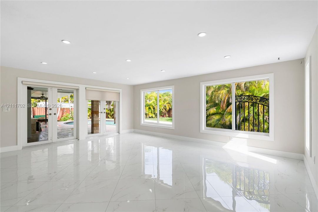 Open-concept interior featuring large-format polished stone-finish tile flooring, recessed ceiling lighting, dual sliding glass doors, and expansive picture windows