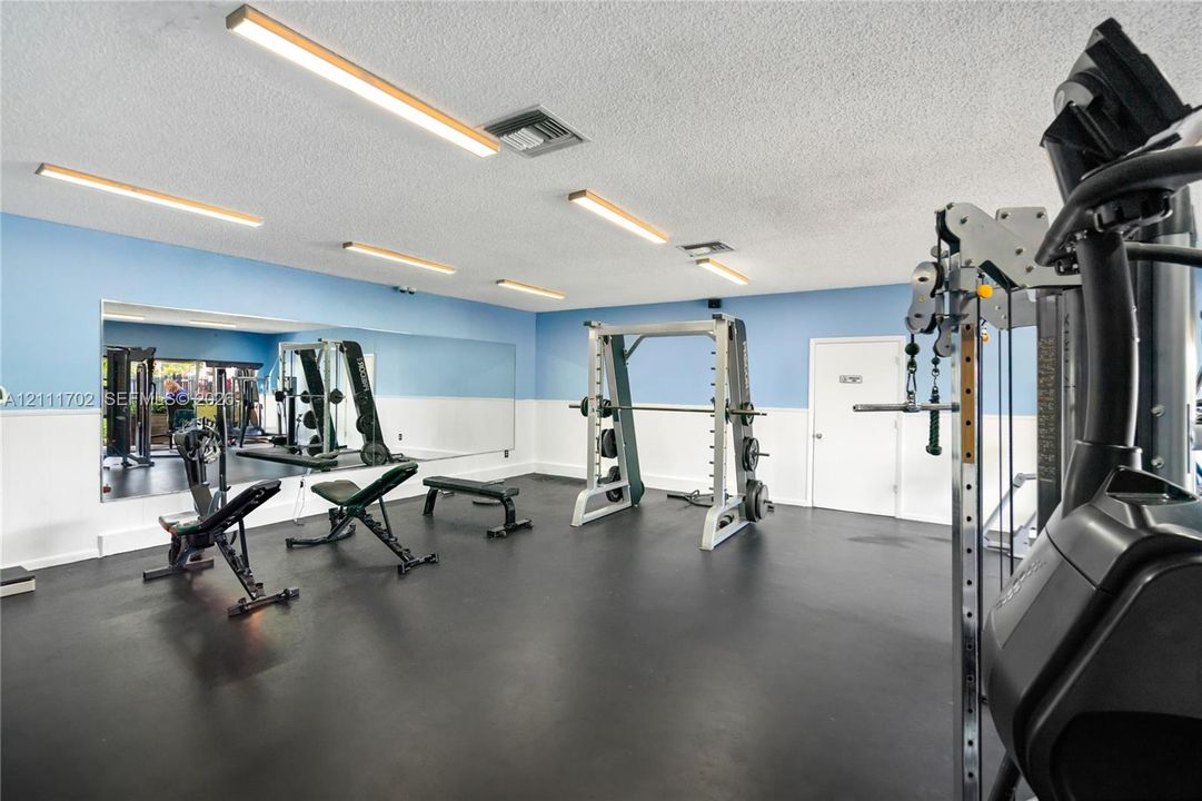 Spacious room featuring floor-to-ceiling wall mirror, impact-resistant rubber flooring, and multiple linear LED overhead light fixtures