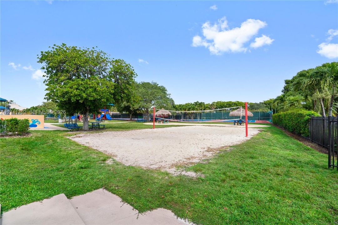 Outdoor recreation area featuring a sand volleyball court, manicured lawn, and mature shade trees