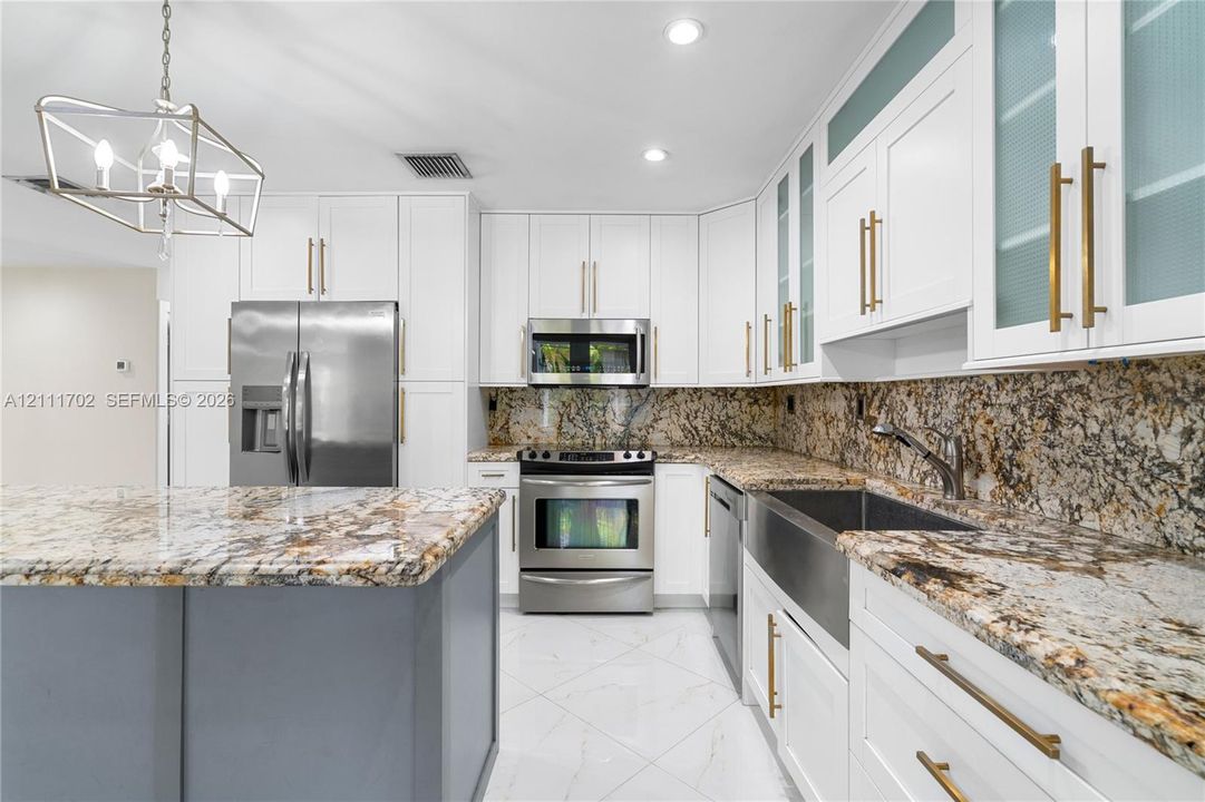 Kitchen featuring white shaker cabinetry, stone countertops, stainless steel farmhouse sink, brushed gold hardware, and a center island with contrasting gray cabinetry