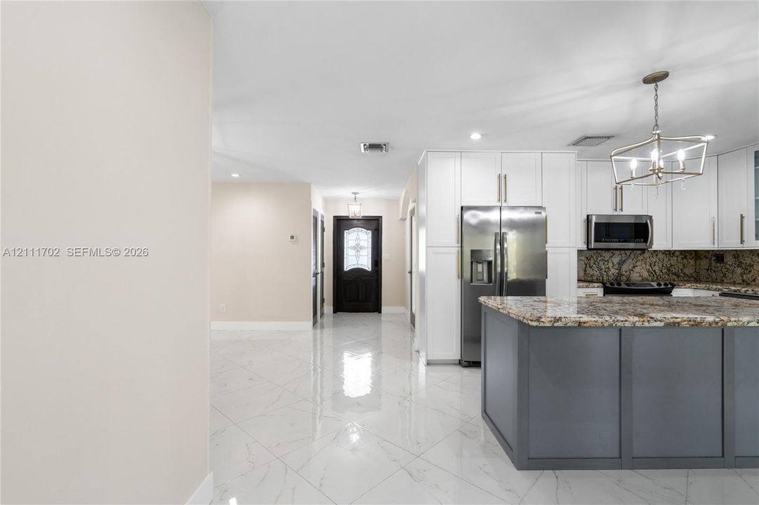 Kitchen featuring white cabinetry, a center island with a dark-toned finish, stone-surfaced countertops, a stainless steel refrigerator, and recessed lighting