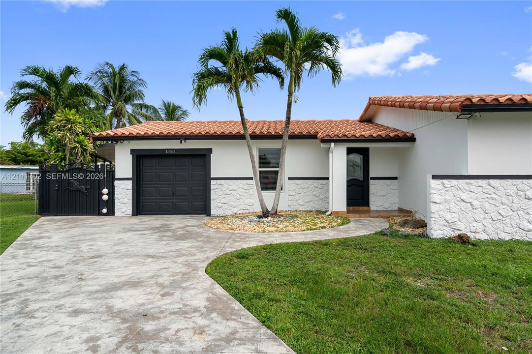 Single-story exterior featuring white stucco walls, decorative stone veneer, terracotta roof tiles, an attached garage, and a gated side entrance
