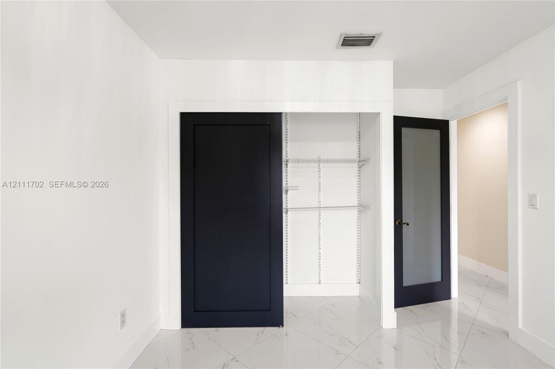 Custom closet featuring sliding doors, white-finish wire shelving, and stone-pattern tile flooring, complemented by a solid-core interior door with a frosted glass panel