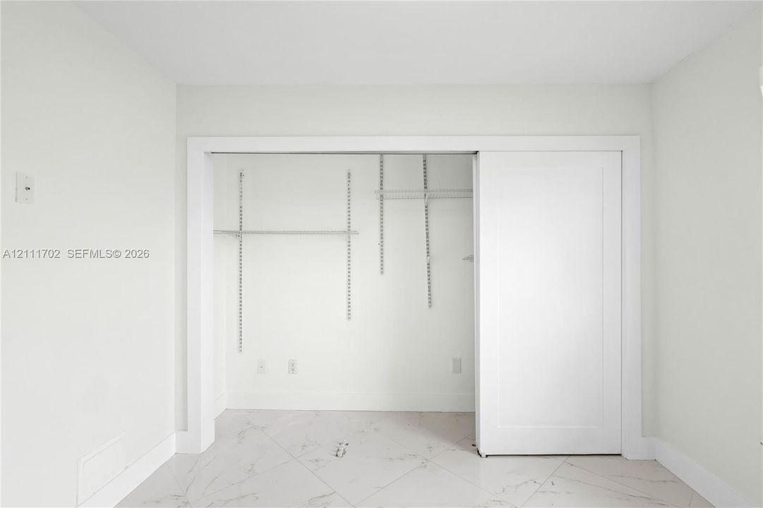 Storage space featuring white sliding doors and interior adjustable wire shelving, set against stone-finish tile flooring