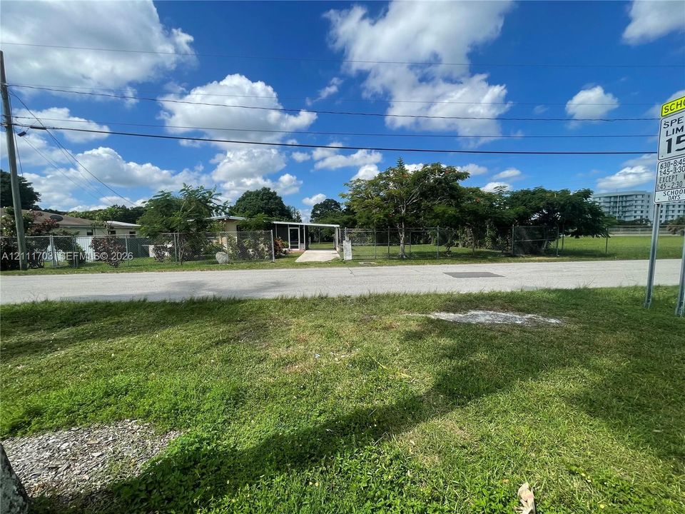 Single-story residence featuring a paved entryway, chain-link perimeter fencing, and mature trees