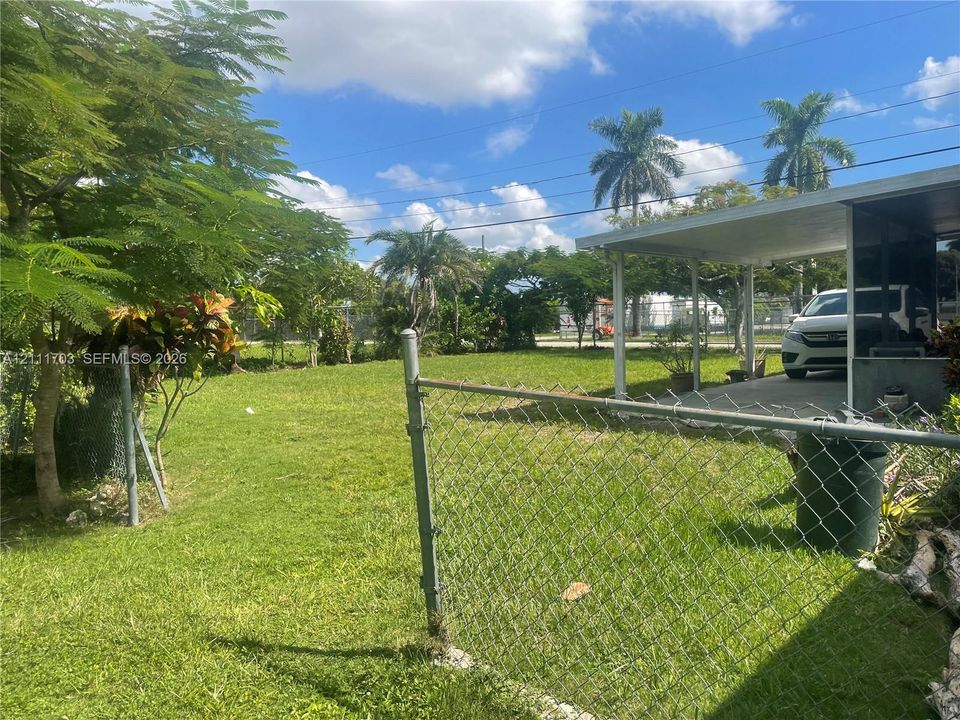 Expansive backyard featuring a chain-link fence, concrete patio covering, and mature trees