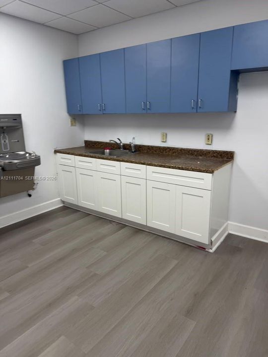 Work area featuring blue upper cabinetry, white lower cabinetry, stone-finish countertops, stainless steel sink with faucet, and wood-finish flooring