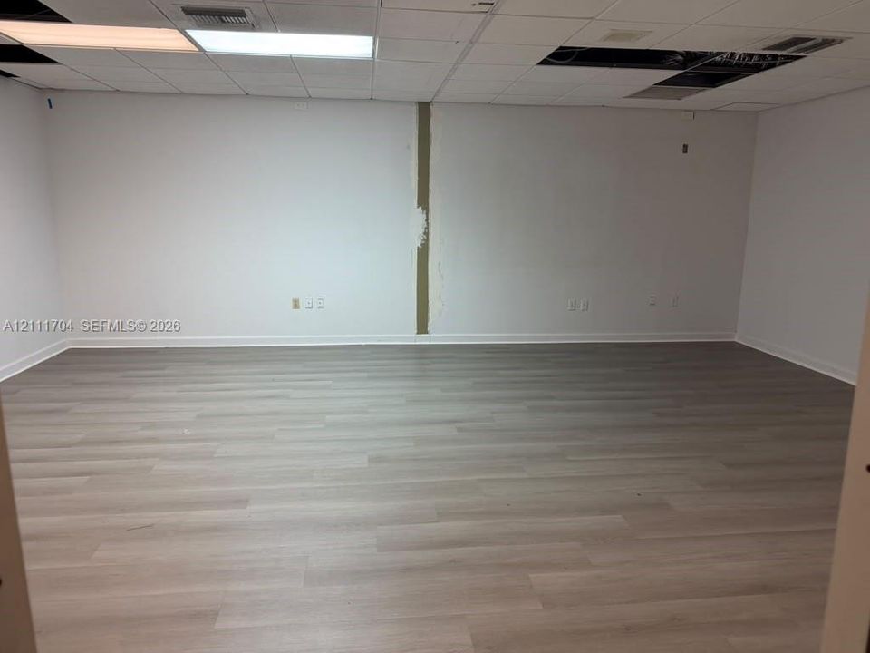 Interior space featuring wood-finish flooring, white walls, and a drop ceiling with recessed panel lighting