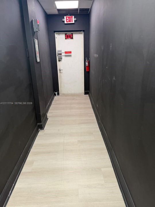 Hallway featuring light-toned wood-finish flooring, dark-painted walls, and a recessed ceiling lighting fixture