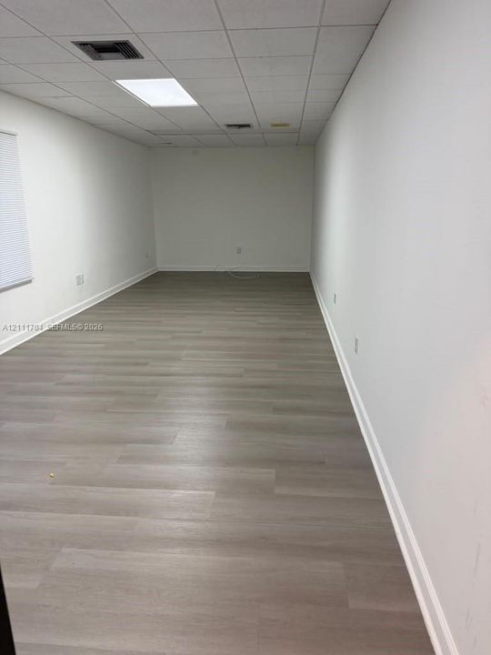 Open interior space featuring wood-finish flooring, neutral walls, and a drop ceiling with recessed panel lighting