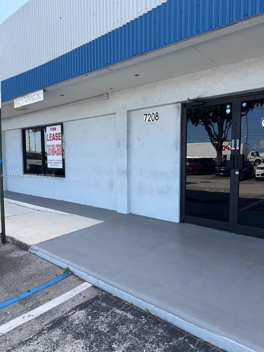 Commercial storefront exterior featuring corrugated metal roofing, dual-pane glass entrance doors, and a painted concrete sidewalk