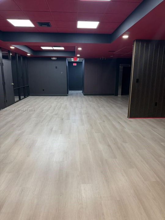 Open-concept space featuring light wood-finish flooring, recessed square ceiling lighting, matte black walls, and a vertical-slatted accent wall