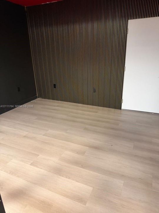 Interior room featuring vertical wood slat accent wall paneling, light-tone wood-finish flooring, and solid-core interior door