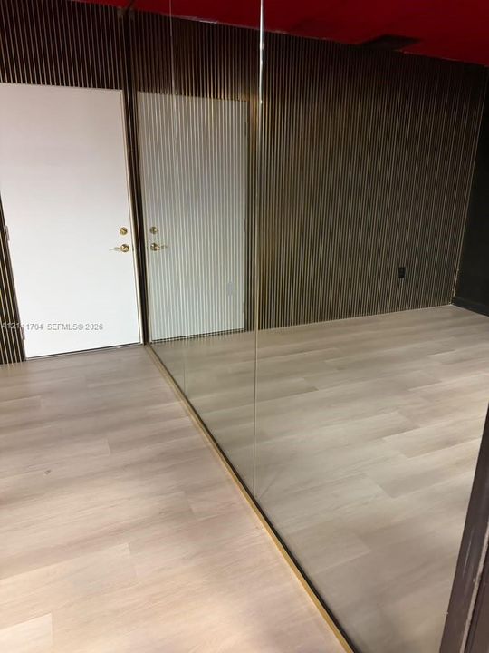 Slatted wood-tone wall paneling paired with light-toned wood-finish flooring and floor-to-ceiling glass wall partition