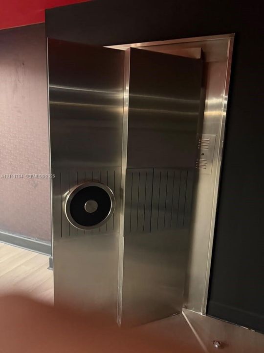 Industrial-style stainless steel vault door featuring a circular locking mechanism, linear textured paneling, and a reinforced metal frame