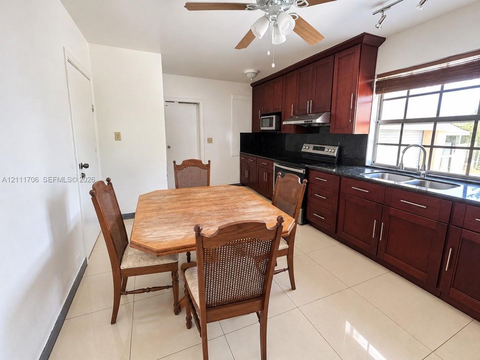 Kitchen featuring cherry-finish cabinetry, dark stone countertops, stainless steel appliances, large-format tile flooring, and a multi-pane window