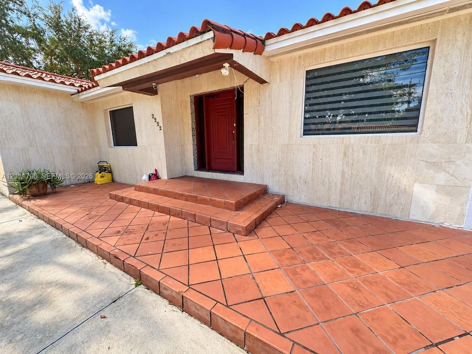 Exterior entrance featuring natural stone wall cladding, a terracotta tile porch, a low-profile overhang with a barrel-tile roof, and a solid-core entry door