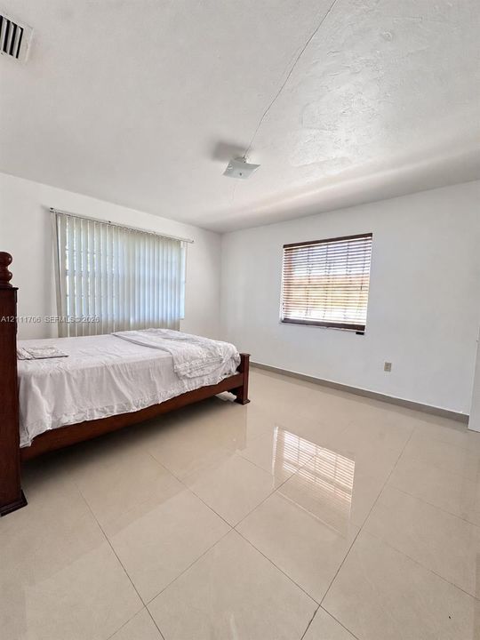 Spacious room with polished tile flooring, neutral wall finishes, vertical blinds, and horizontal slatted window treatments